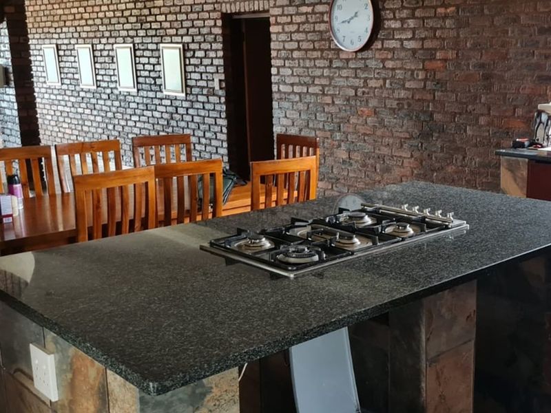 Open plan kitchen and dining area featuring a central granite island with a built-in gas hob and rustic exposed brick walls.