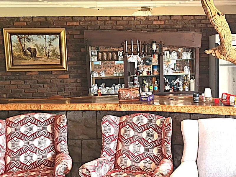 A rustic bar area featuring a natural wood slab countertop, exposed brick wall, and built-in mirrored shelving for display.