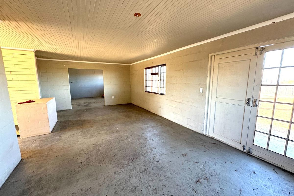 An unfinished interior space featuring exposed concrete block walls, concrete flooring, and a timber-paneled ceiling with access to an adjacent room.