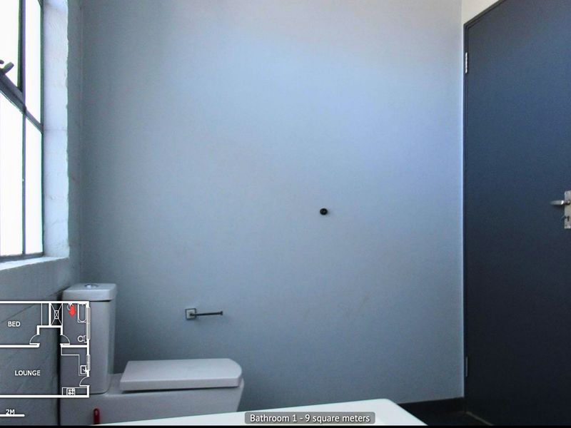 A minimalist bathroom featuring a toilet, industrial-style window, and a dark interior door.