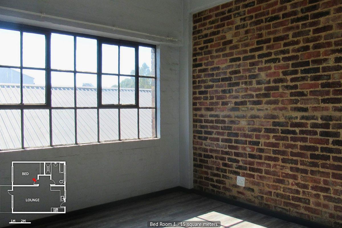 A bright bedroom featuring an exposed brick wall, industrial-style steel-framed windows, and modern laminate flooring.