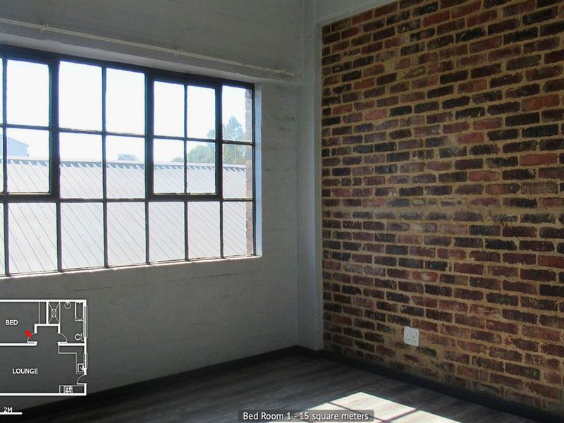 A bright bedroom featuring an exposed brick wall, industrial-style steel-framed windows, and modern laminate flooring.