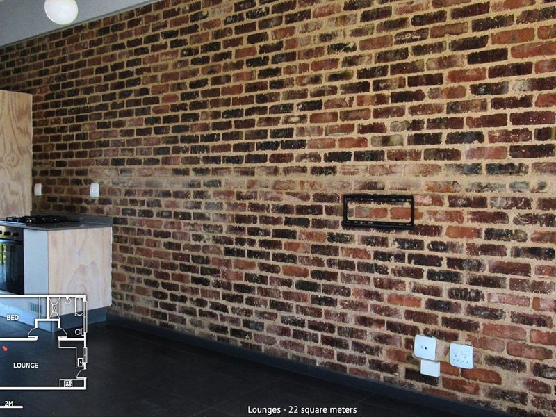 Open plan living area featuring an exposed brick feature wall, tiled flooring, and a compact kitchen unit with built-in oven and hob.