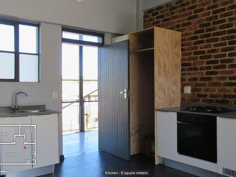 Compact kitchen featuring exposed brickwork, built-in oven with gas hob, stainless steel sink, and unfinished plywood cabinetry, leading to an outdoor balcony area.