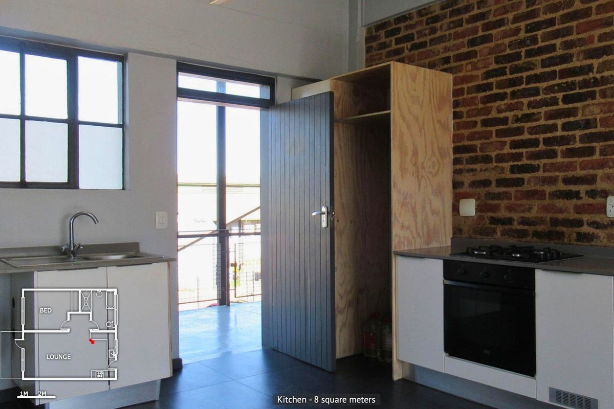 Compact kitchen featuring exposed brickwork, built-in oven with gas hob, stainless steel sink, and unfinished plywood cabinetry, leading to an outdoor balcony area.