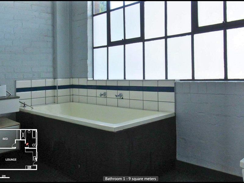 Bathroom featuring a built-in bathtub, industrial-style steel frame windows, and exposed brick walls.