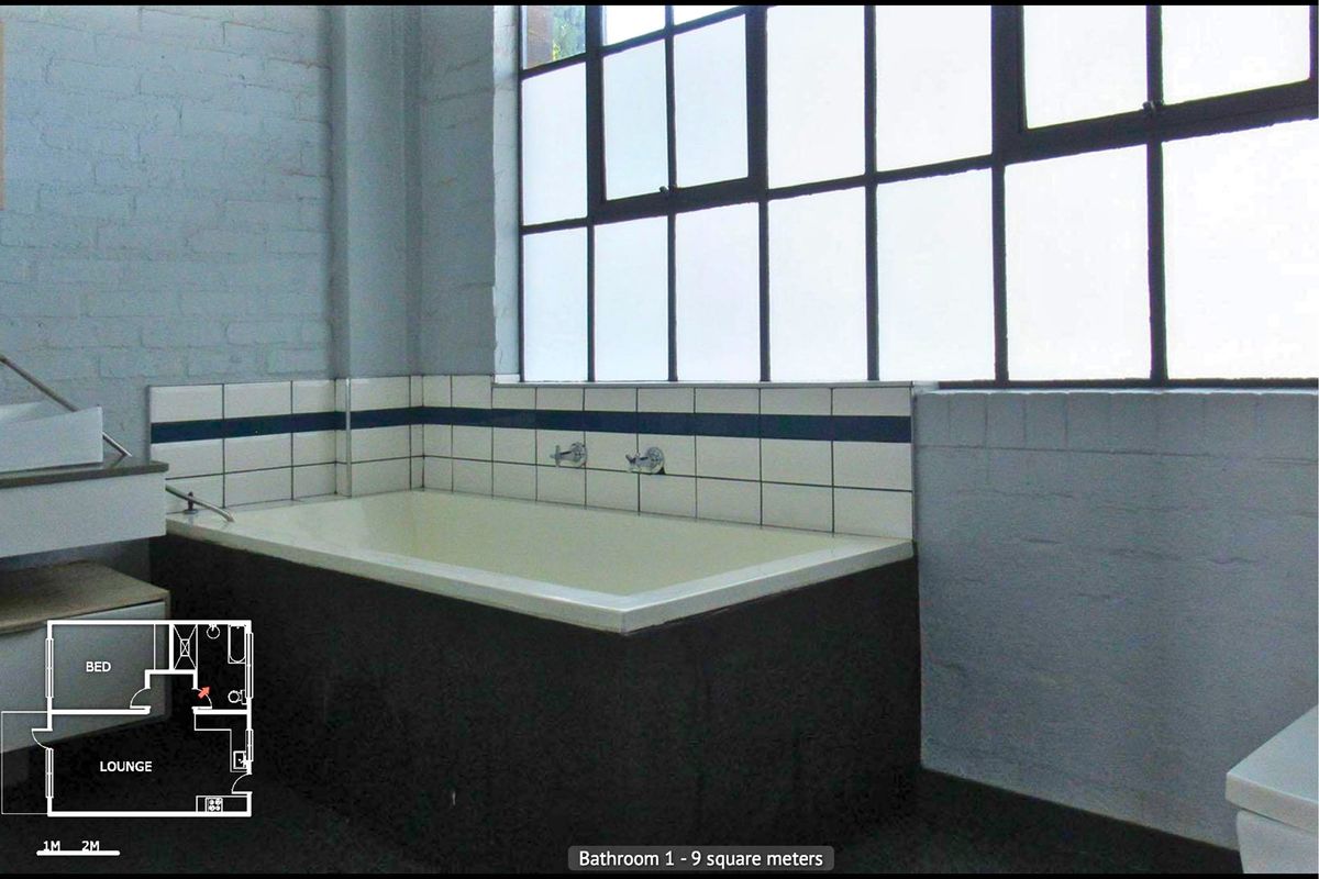 Bathroom featuring a built-in bathtub, industrial-style steel frame windows, and exposed brick walls.