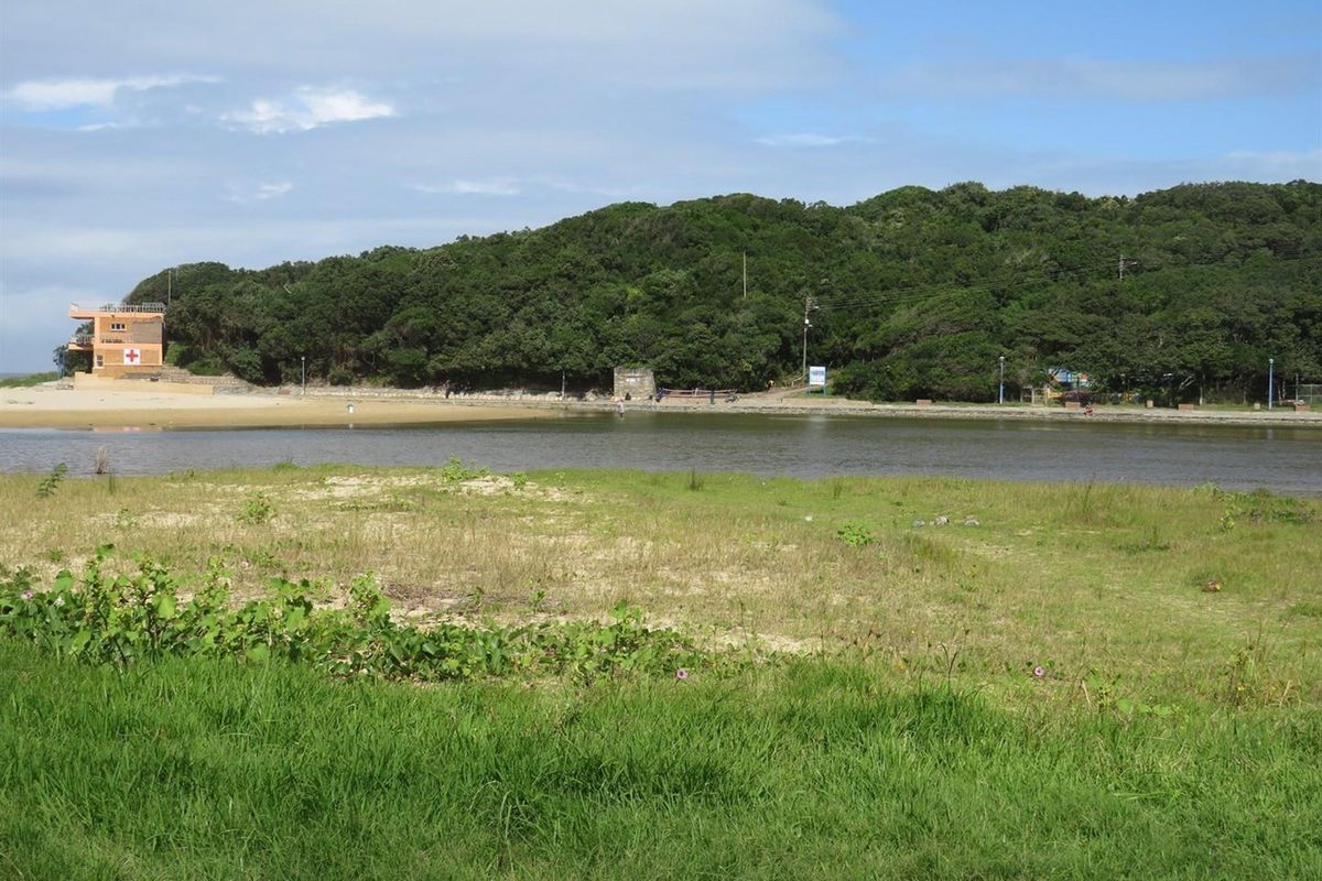 A scenic view of a coastal lagoon and natural landscape, featuring a lifeguard tower in the distance and surrounding greenery.