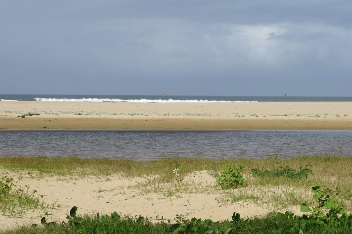A scenic view of the coastal landscape, featuring a sandy beach, natural waterway, and ocean horizon.