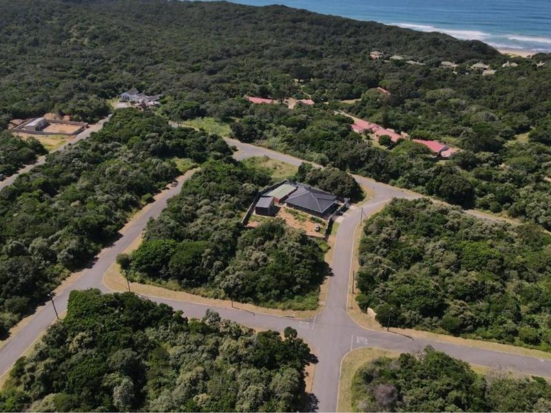 Aerial view of a residential plot situated within a coastal estate, featuring established vegetation and proximity to the coastline.