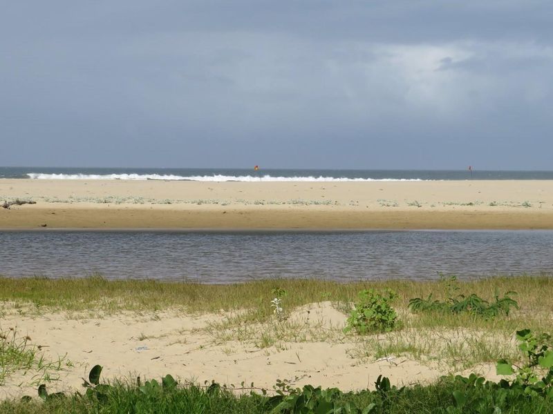 A scenic view of the coastal landscape, featuring a sandy beach, natural waterway, and ocean horizon.