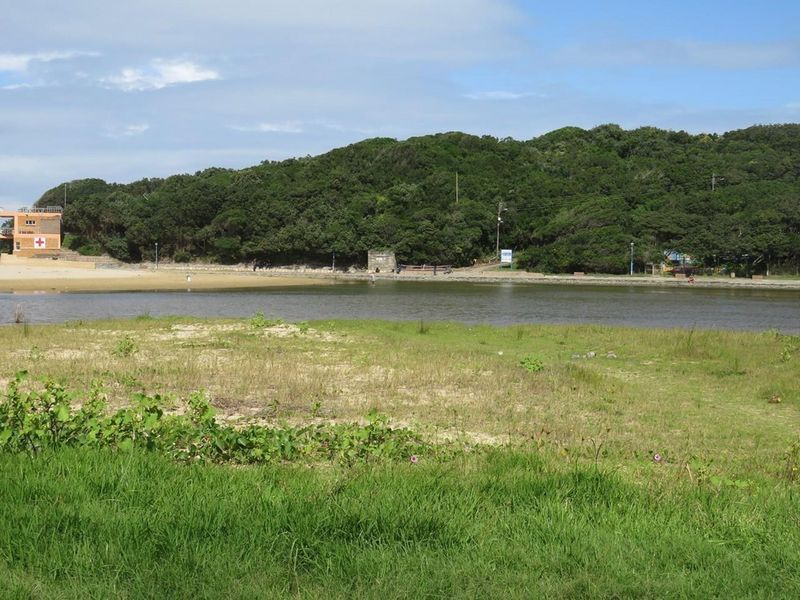A scenic view of a coastal lagoon and natural landscape, featuring a lifeguard tower in the distance and surrounding greenery.