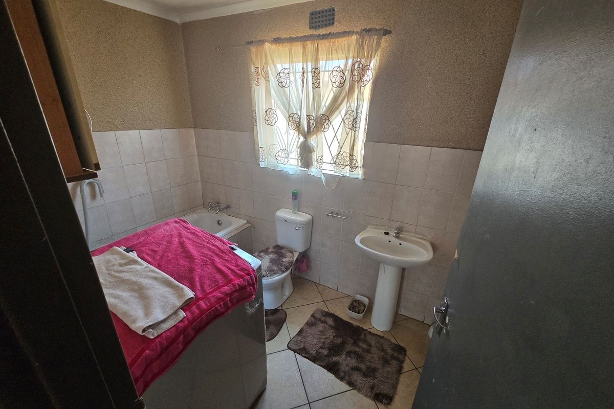 A functional bathroom featuring a pedestal basin, toilet, and built-in bathtub with tiled splashbacks and a window with security bars.