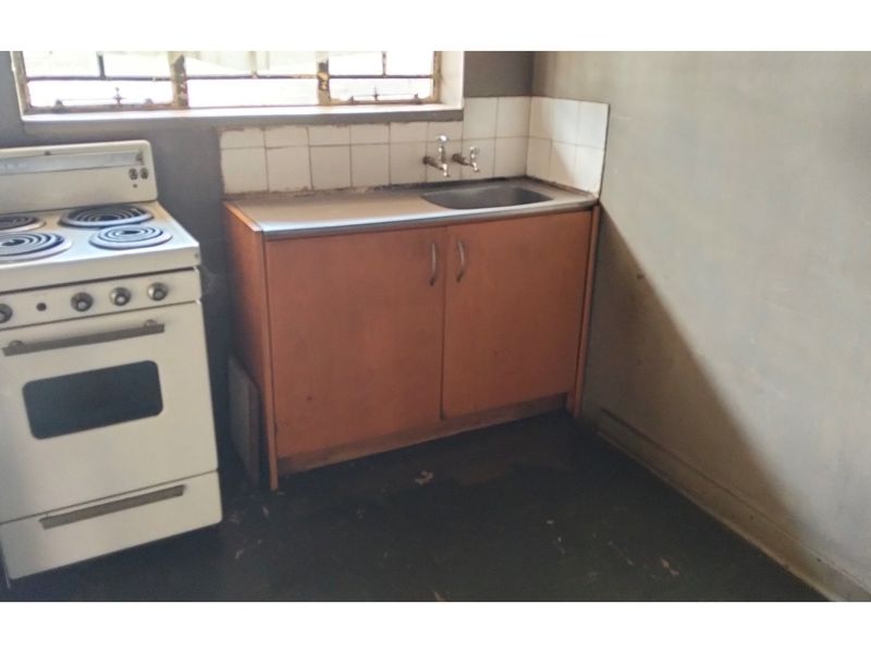 A basic, dated kitchen area featuring a freestanding stove, single sink, and simple base cabinetry with unfinished wall surfaces.