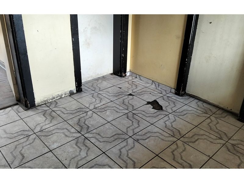 A vacant hallway area featuring patterned ceramic floor tiles that show visible signs of damage and wear.