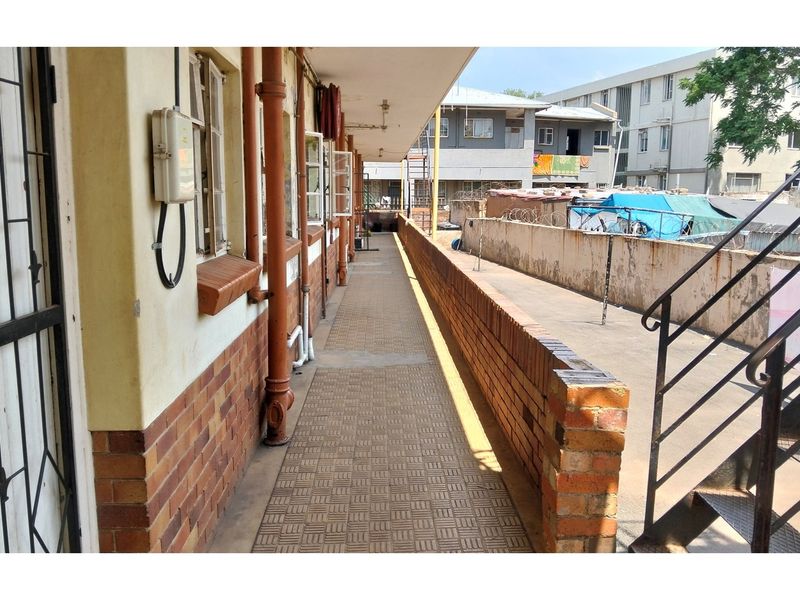 An exterior walkway or balcony area featuring brick wall finishes, a metal staircase, and exposed utility piping in an apartment complex setting.