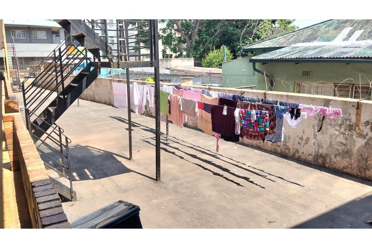 Rear exterior area featuring an asphalt surface, perimeter wall with security wire, and an external metal staircase.