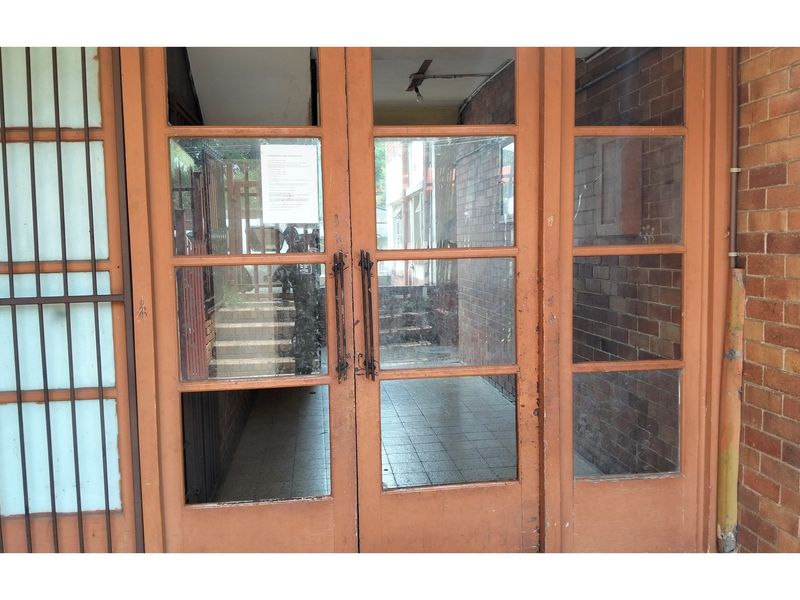 Entrance area featuring timber-framed glass doors, exposed brick walls, and tiled flooring, showing signs of wear and requiring maintenance.