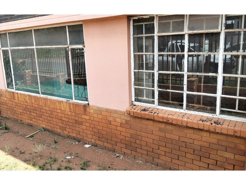 Exterior view of the apartment facade featuring brickwork and steel-framed windows with security bars, showing signs of wear and maintenance requirements.