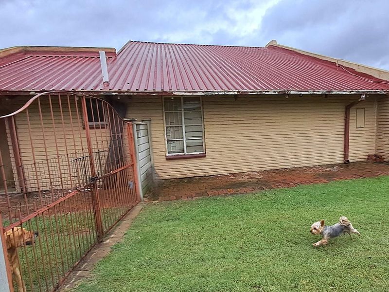 Rear view of the property featuring a corrugated metal roof, brick exterior walls, and a fenced garden area.