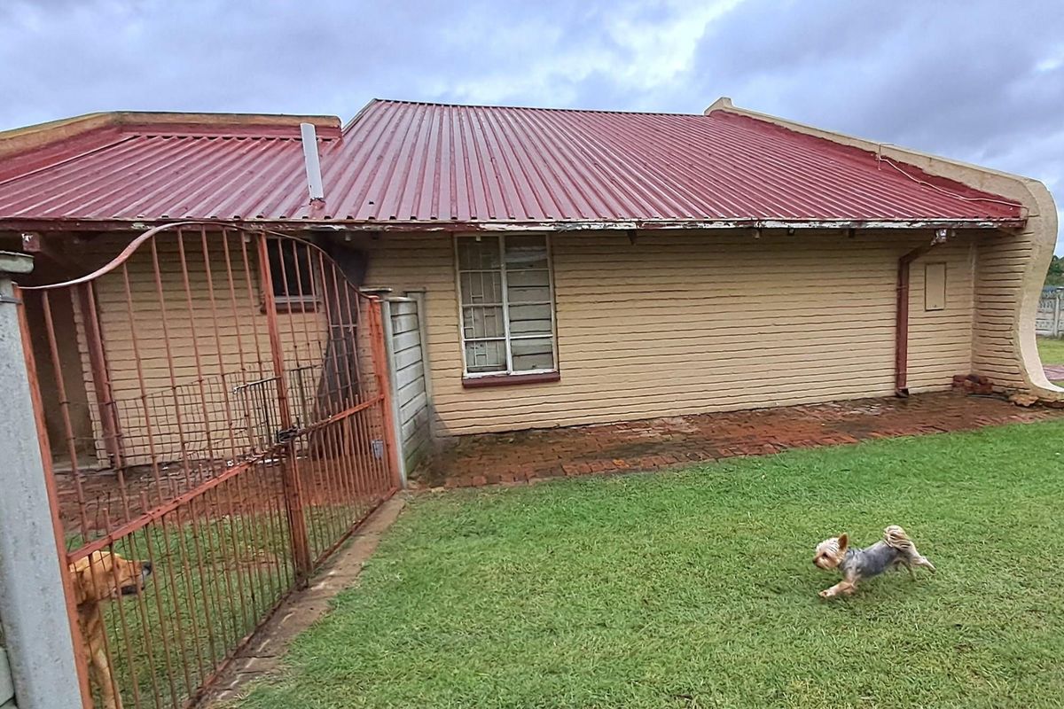 Rear view of the property featuring a corrugated metal roof, brick exterior walls, and a fenced garden area.