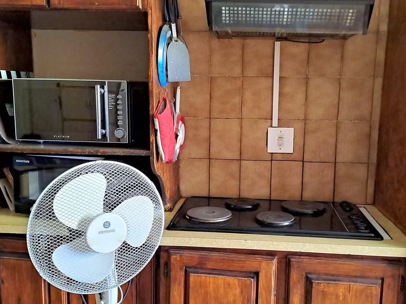 A dated kitchen cooking area featuring a built-in electric hob, extractor fan, and tiled splashback with traditional wooden cabinetry.