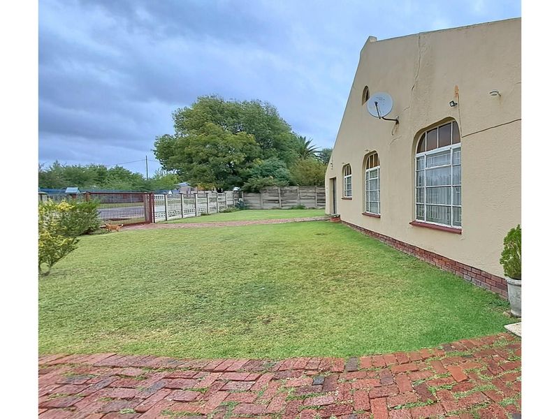 A view of the rear garden featuring a lawn, brick paved pathway, and the side elevation of the house with arched windows.
