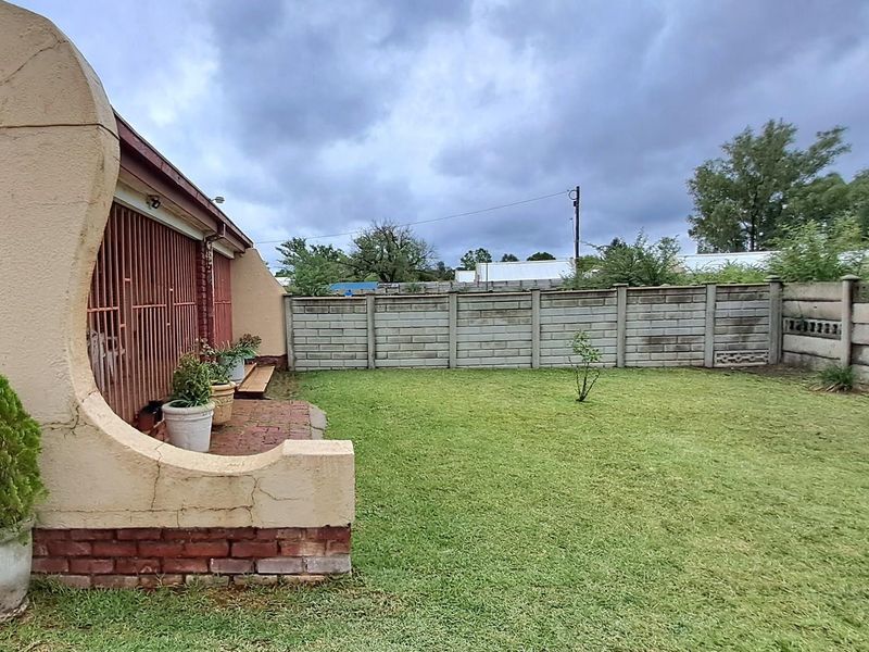 A rear garden area featuring a lawn, a precast concrete boundary wall, and a covered patio area with security bars.