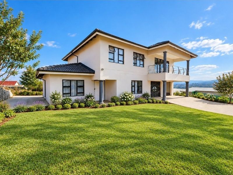 A well-maintained two-story residential property featuring a tiled roof, a spacious balcony with metal balustrades, and a neatly landscaped front garden.