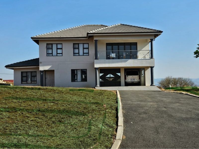 A modern double-story residential house featuring a tiled roof, a front balcony with stainless steel balustrades, and an integrated double garage with a paved driveway.