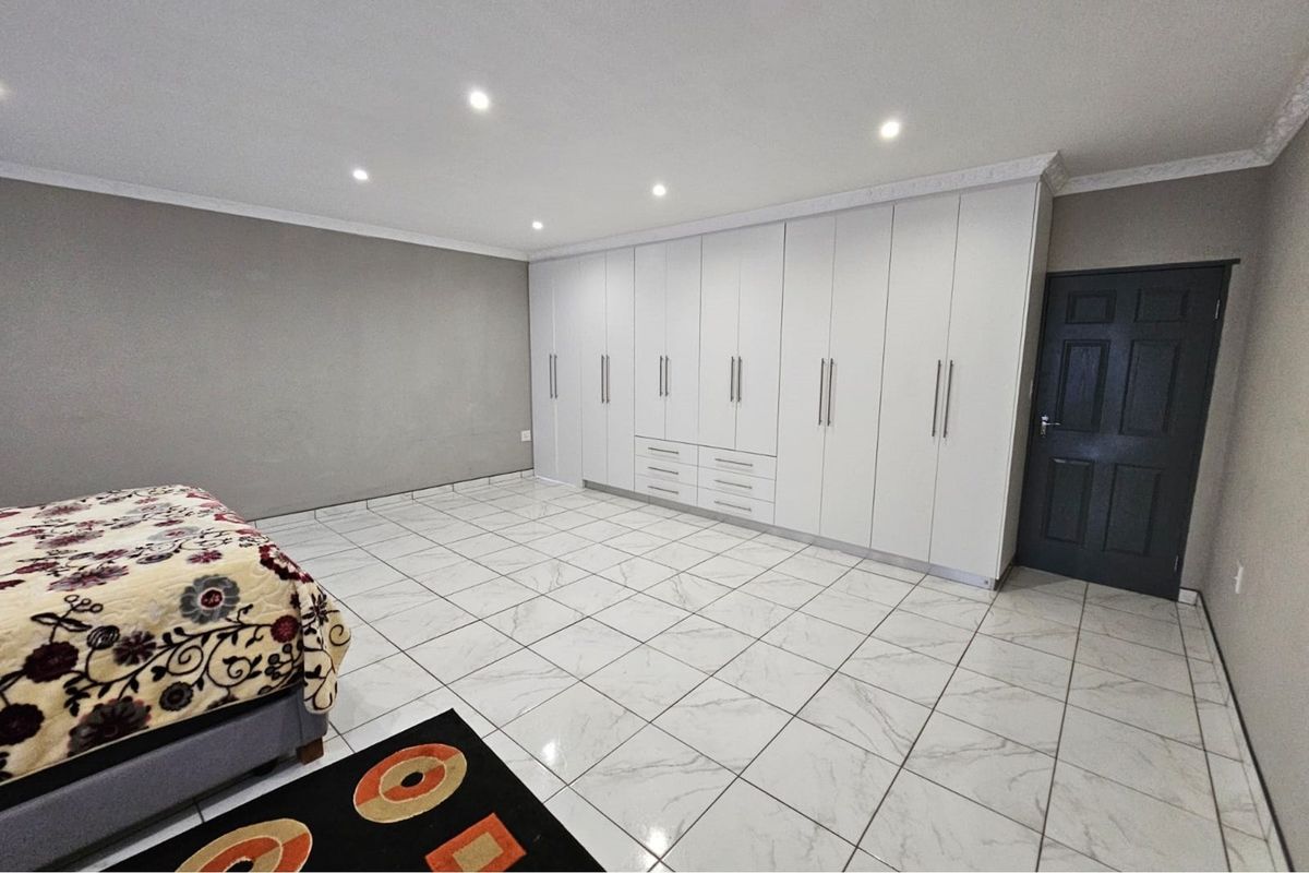 Spacious bedroom featuring extensive white built-in cupboards, modern marble-look tiled flooring, and recessed downlighting.
