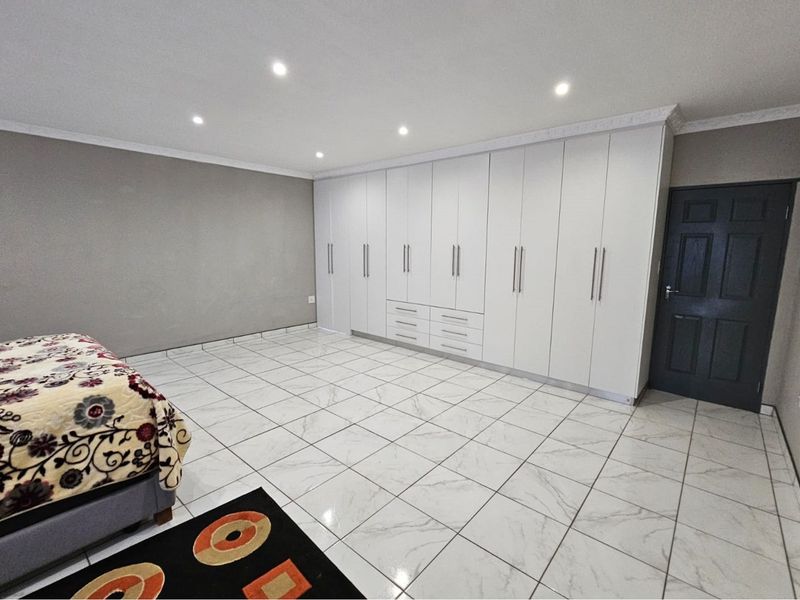 Spacious bedroom featuring extensive white built-in cupboards, modern marble-look tiled flooring, and recessed downlighting.