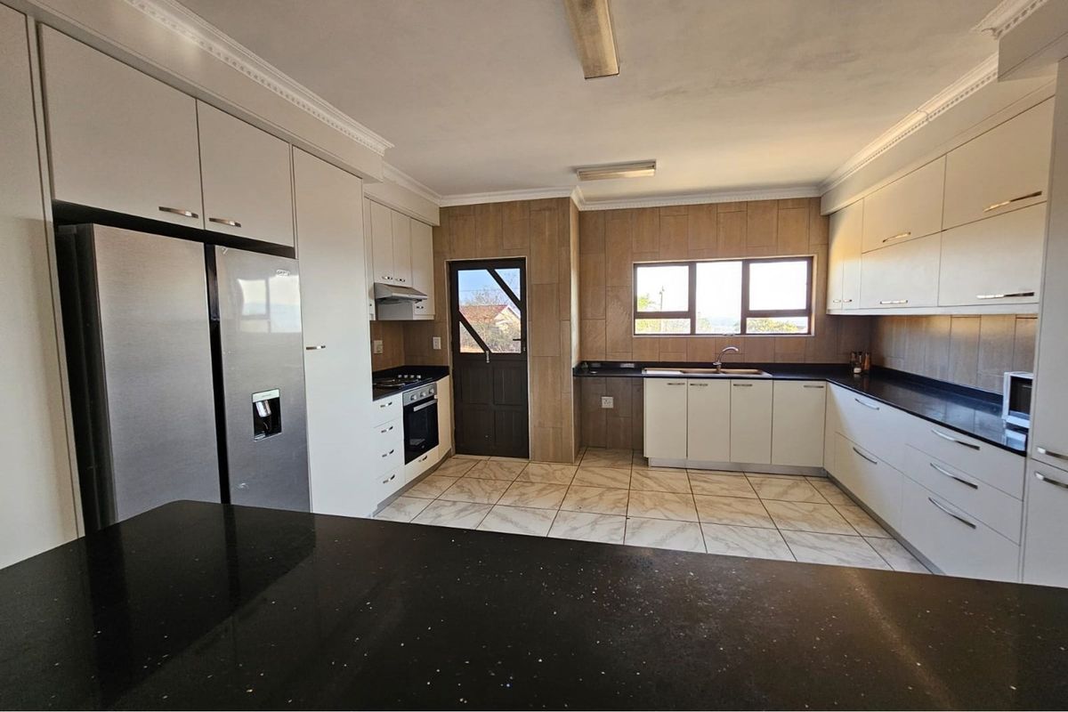 A spacious, modern kitchen featuring white cabinetry, dark granite countertops, built-in appliances, and tiled flooring with direct access to the exterior.
