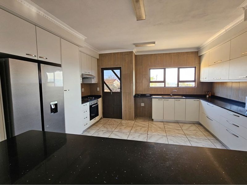 A spacious, modern kitchen featuring white cabinetry, dark granite countertops, built-in appliances, and tiled flooring with direct access to the exterior.