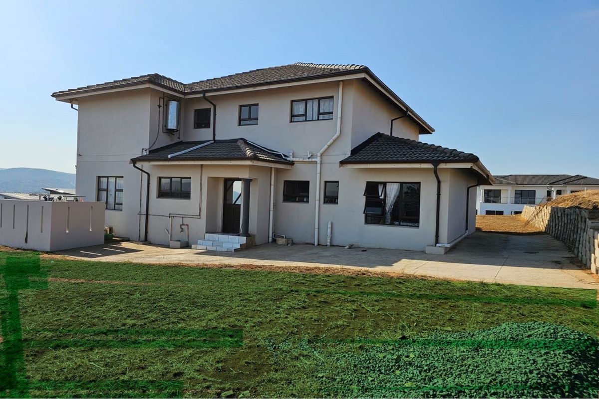 Rear view of a double-storey residential house featuring a concrete patio, tiled roof, and aluminium window frames set against a landscaped garden area.