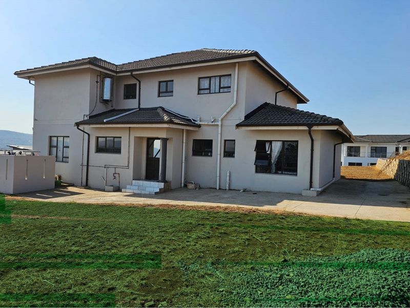 Rear view of a double-storey residential house featuring a concrete patio, tiled roof, and aluminium window frames set against a landscaped garden area.