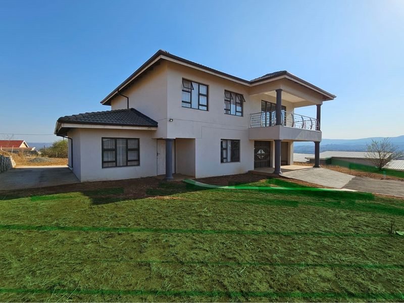 A two-story residential property featuring a balcony, tiled roof, and concrete driveway, set against a clear sky with surrounding landscape.