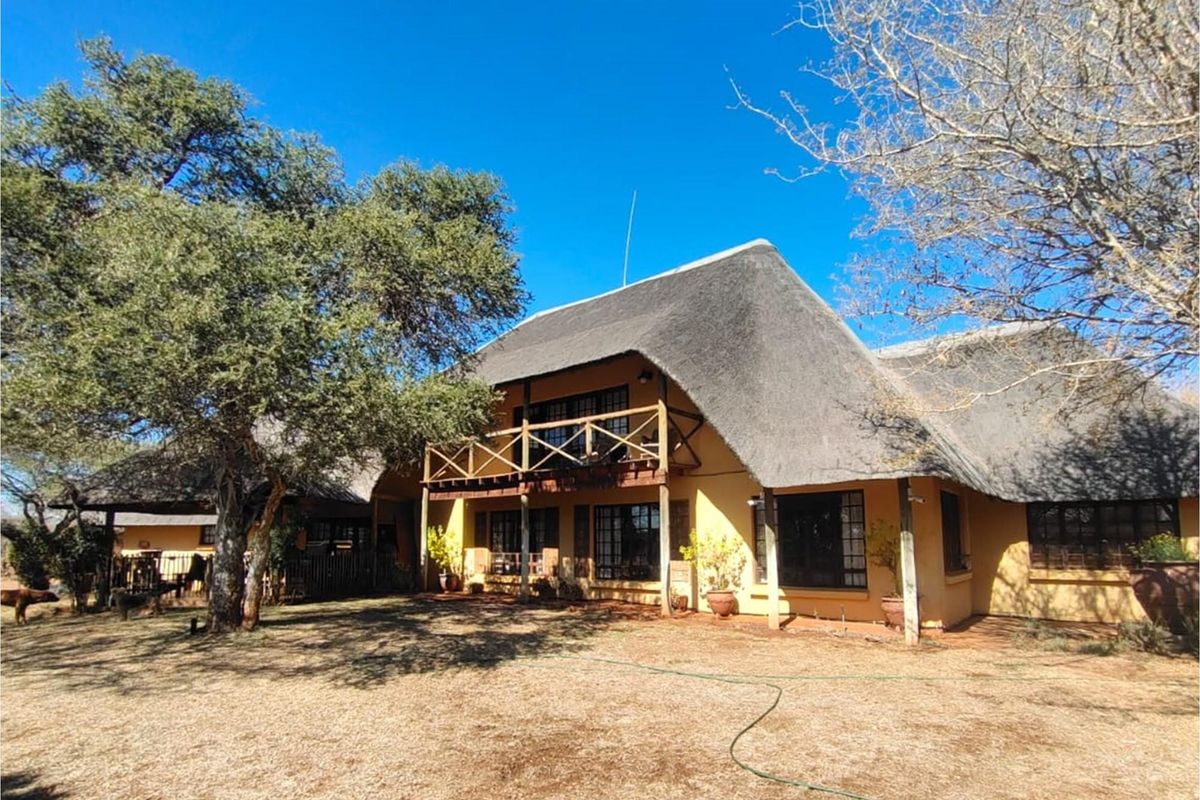 A rear view of a traditional house featuring a large thatched roof, timber balcony, and expansive garden area.