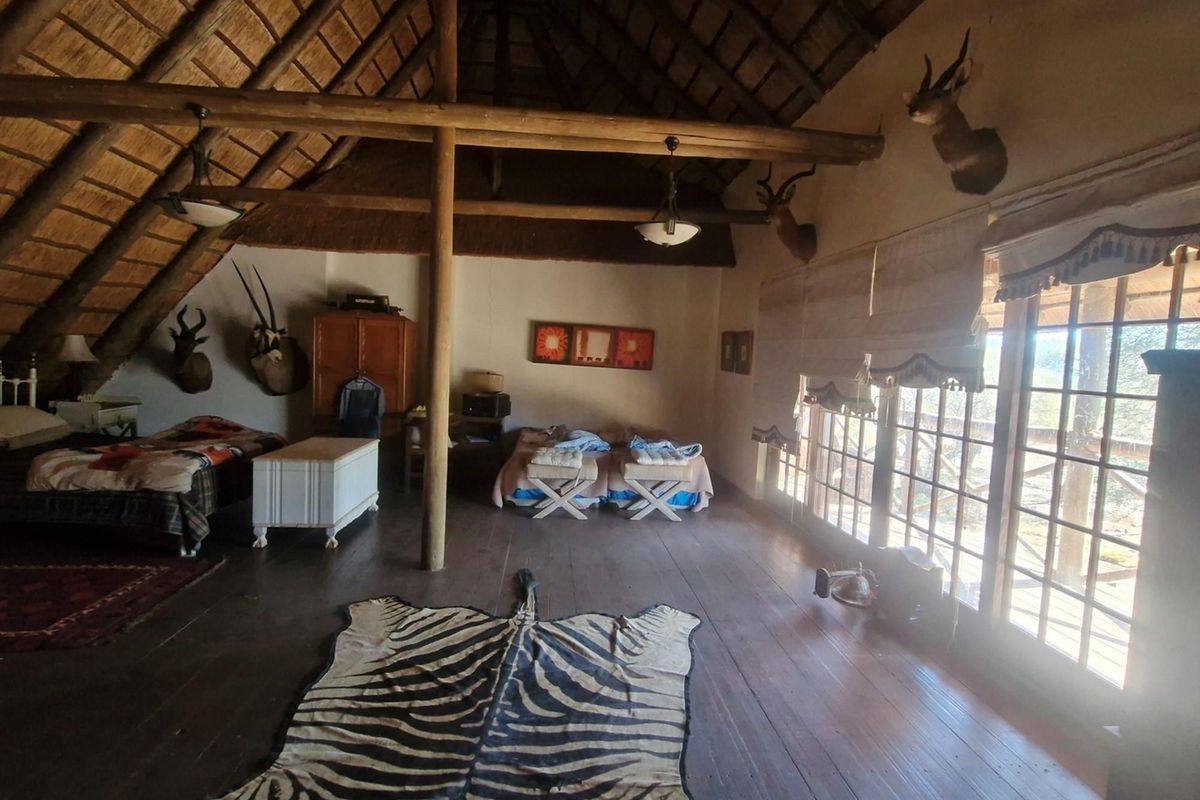 Spacious bedroom featuring a traditional thatched roof with exposed timber beams, wooden flooring, and large glass doors leading to an outdoor area.