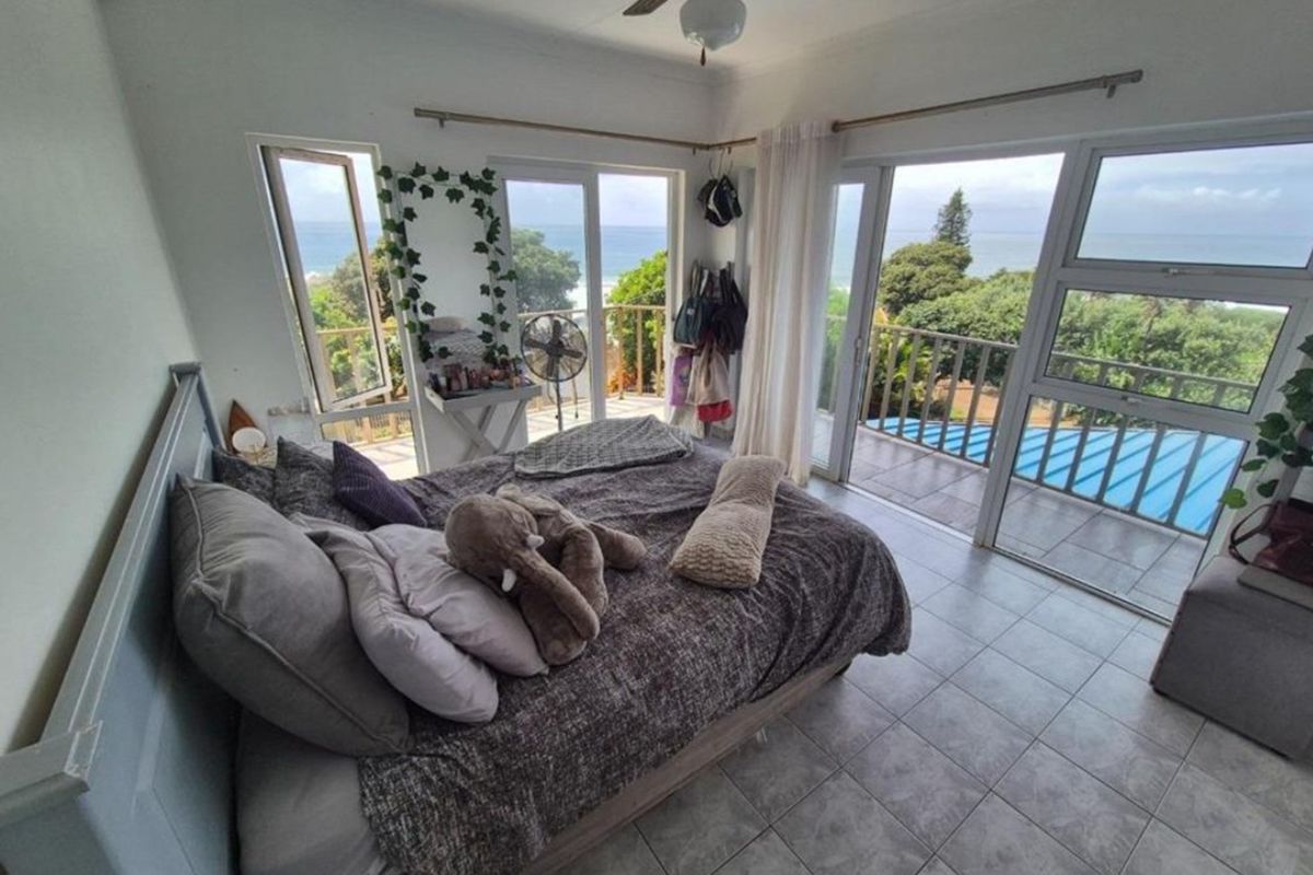 A bedroom featuring tiled flooring, a ceiling fan, and large sliding glass doors that open onto a balcony with ocean views.