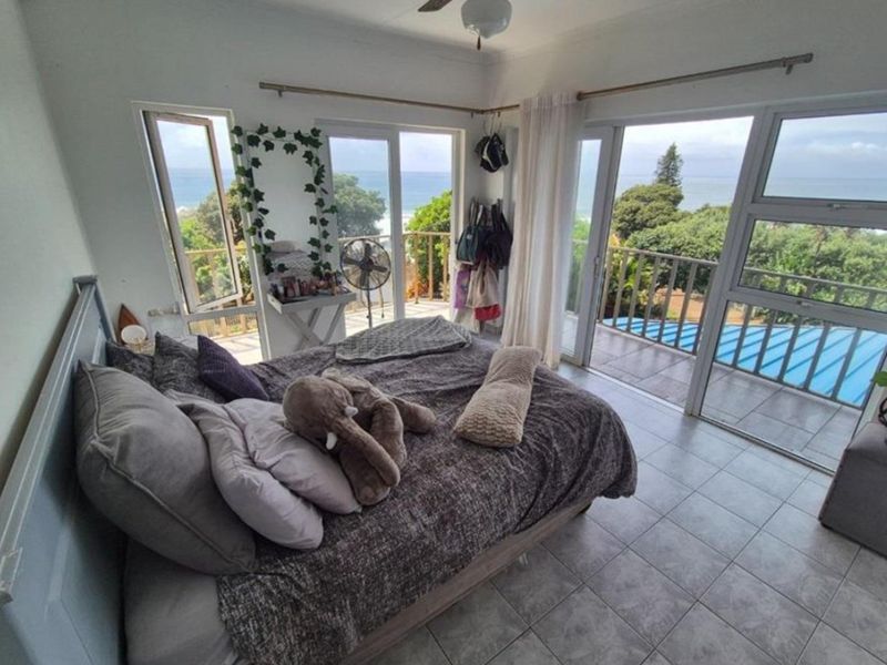 A bedroom featuring tiled flooring, a ceiling fan, and large sliding glass doors that open onto a balcony with ocean views.