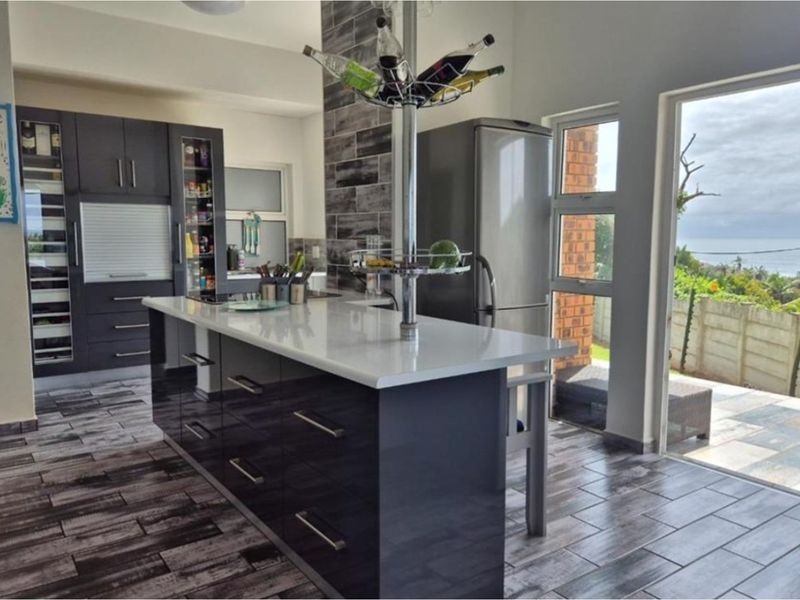 Modern kitchen featuring a central island with stone countertops, dark cabinetry, and tiled flooring, with direct access to an outdoor patio area.