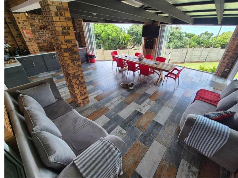 Spacious covered patio featuring exposed brick pillars, tiled flooring, and folding glass doors, creating a seamless transition to the outdoor garden area.