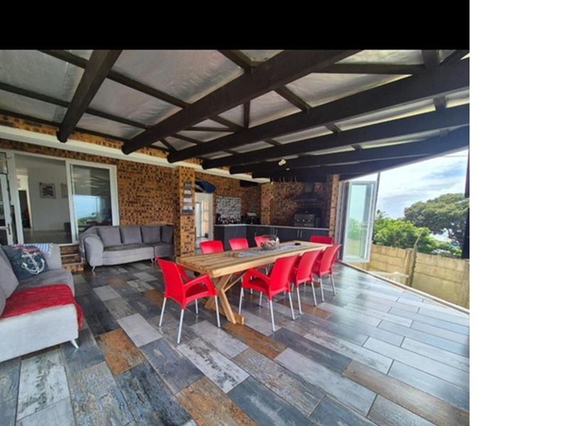Spacious covered patio featuring exposed timber beams, facebrick walls, tiled flooring, and a built-in braai area, perfect for outdoor entertaining.