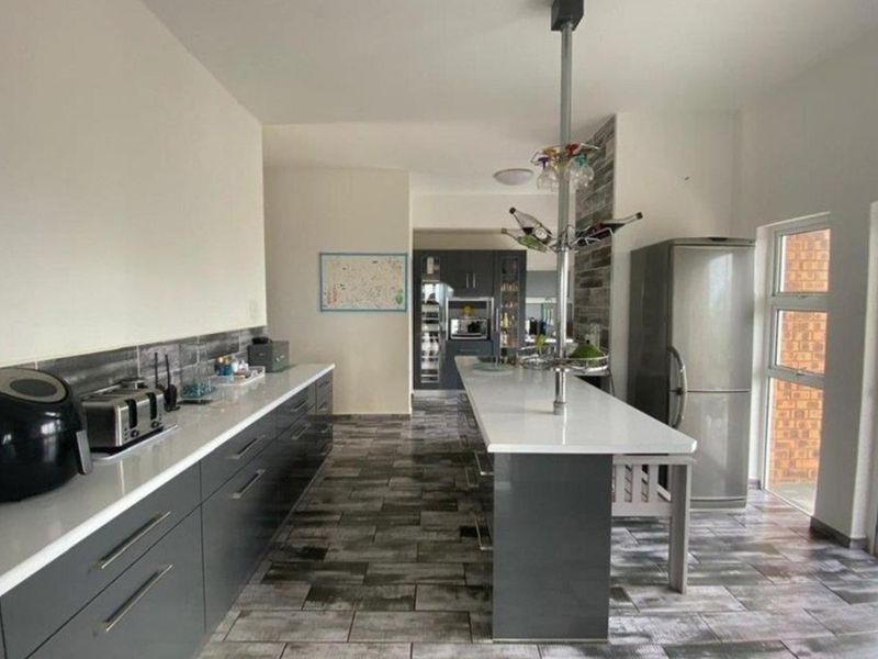 Modern kitchen featuring dark grey cabinetry, white stone countertops, a central island, and tiled flooring with a sleek, contemporary finish.