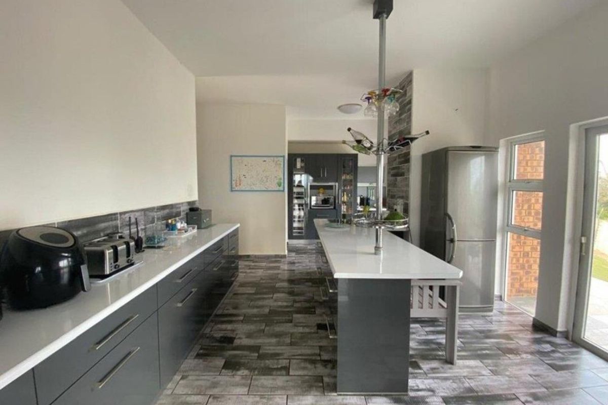 Modern kitchen featuring dark grey cabinetry, white stone countertops, a central island, and tiled flooring with a sleek, contemporary finish.