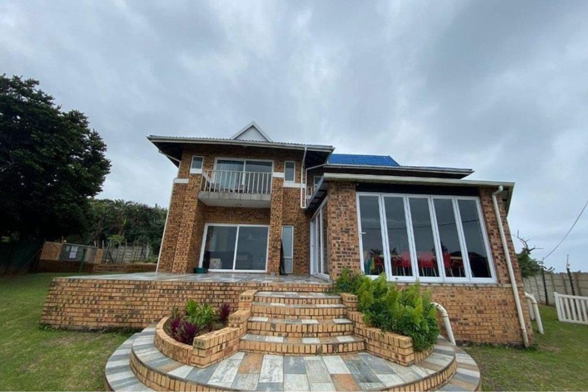 Rear view of a two-story face brick house featuring a tiled patio, balcony, and extensive glass doors leading to the garden.
