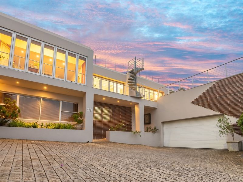 Modern multi-level residential facade featuring a paved driveway, integrated garage, spiral staircase, and upper-level balcony with contemporary architectural finishes.
