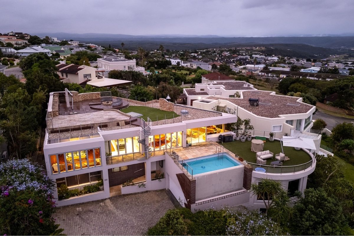 Aerial view of a modern multi-level residence featuring a swimming pool, expansive roof terraces, artificial lawn areas, and a paved driveway.