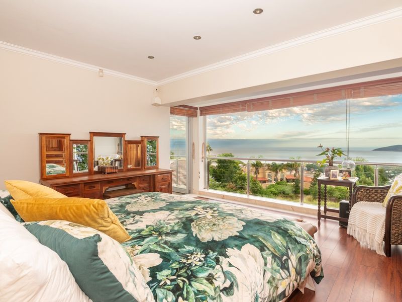 Spacious bedroom featuring laminate flooring, recessed lighting, and expansive sliding glass doors opening to a balcony with panoramic ocean and coastal views.